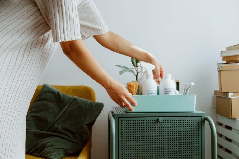 Woman organizing self-care and skincare products in a tray on a small side table at home