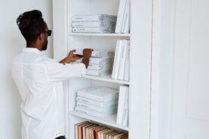 Man organizing books and folded items on white bookshelf at home